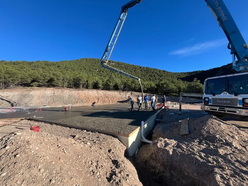 Concrete pump truck pouring a large slab foundation with crew working in a mountain setting